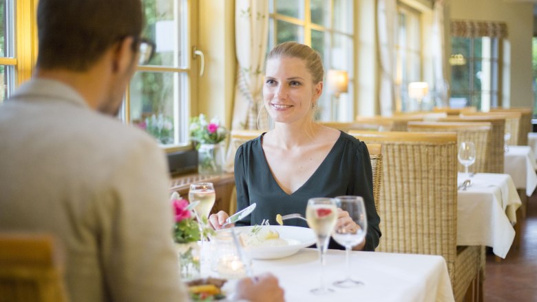 Ein Paar beim Abendessen in einem gemütlichen Restaurant mit großen Fenstern und Kerzenlicht.