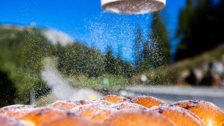 Buchteln werden mit Puderzucker bestreut, im Hintergrund eine Berglandschaft.