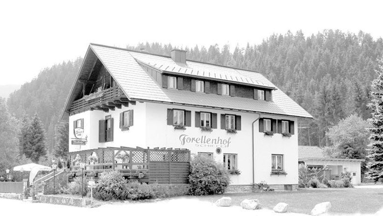 Ein traditionelles Gasthaus mit der Aufschrift 'Forellenhof Schiefer' vor einem Waldhintergrund.