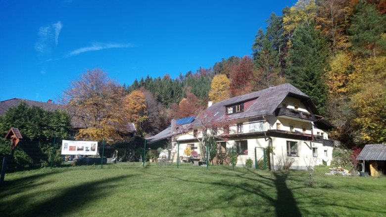 Ein großes Haus mit Schrägdach in einer herbstlichen Waldlandschaft.