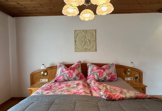Ein gemütliches Schlafzimmer mit einem Doppelbett, floralem Bettzeug und einer Holzdecke. Eine Lampe hängt von der Decke.