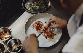 Koch dekoriert ein Gericht mit Lachs und Gemüse auf einem Teller.