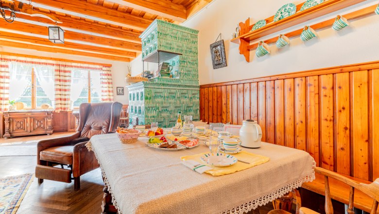 Gemütliches Esszimmer mit Holzmöbeln, gedecktem Tisch und grünem Kachelofen.