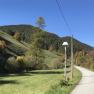Ländliche Straße mit Laterne, umgeben von grünen Hügeln und Bäumen unter blauem Himmel.