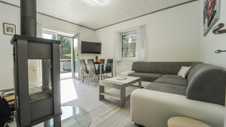 Modernes Wohnzimmer mit Kamin, grauem Sofa, Esstisch und gro&szlig;em Fenster.