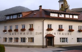 Ein traditionelles Gasthaus mit Blumen an den Fenstern und einem Kirchturm im Hintergrund.