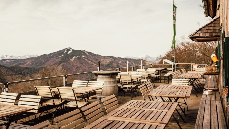 Leere Terrasse mit Holztischen und -stühlen, Berglandschaft im Hintergrund.