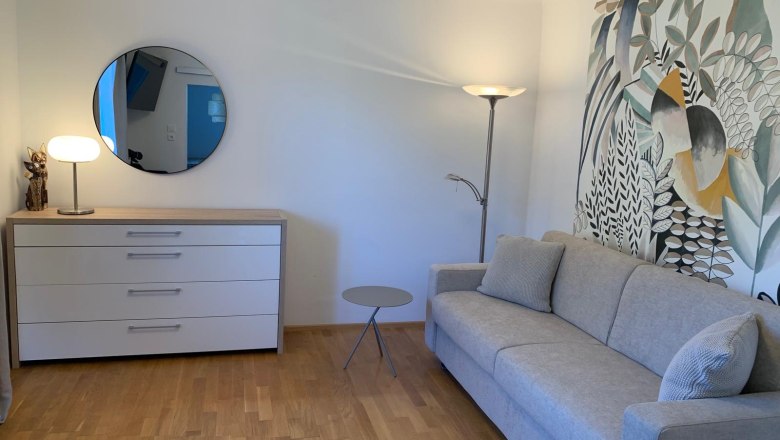 Modernes Wohnzimmer mit grauem Sofa, Kommode, Spiegel und dekorativer Wandkunst.