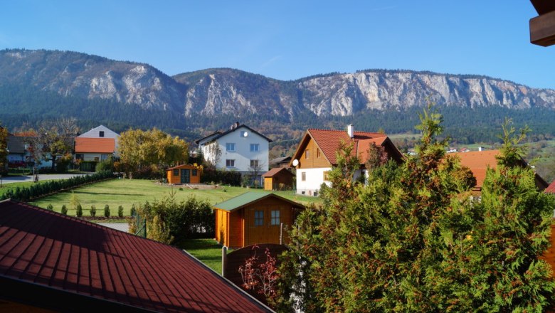 Blick auf Häuser mit roten Dächern und Berge im Hintergrund bei klarem Himmel.