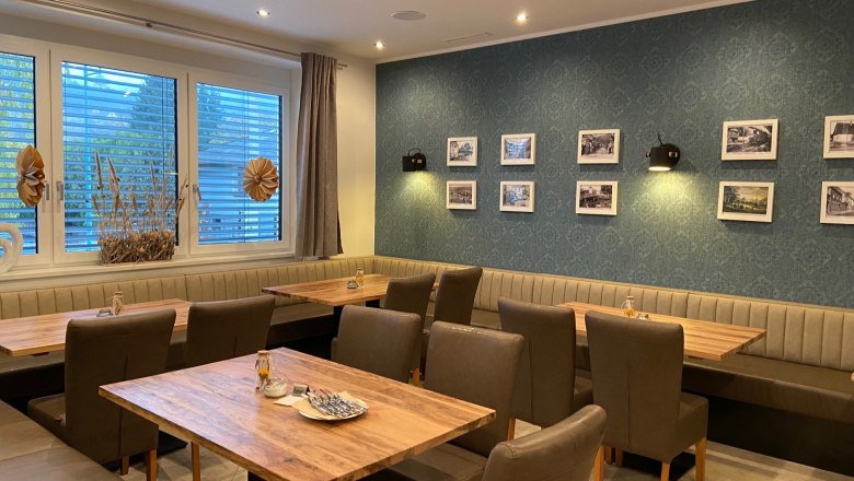 Innenansicht eines Restaurants mit Holztischen, gepolsterten Stühlen und einer Wand mit gerahmten Bildern.