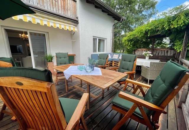 Holzterrasse mit Tisch, gemütlichen Stühlen und Sonnenschutz.