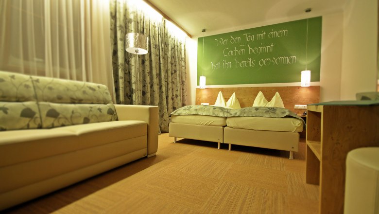 Gemütliches Gästezimmer mit Doppelbett, Sofa und dekorativen Vorhängen.