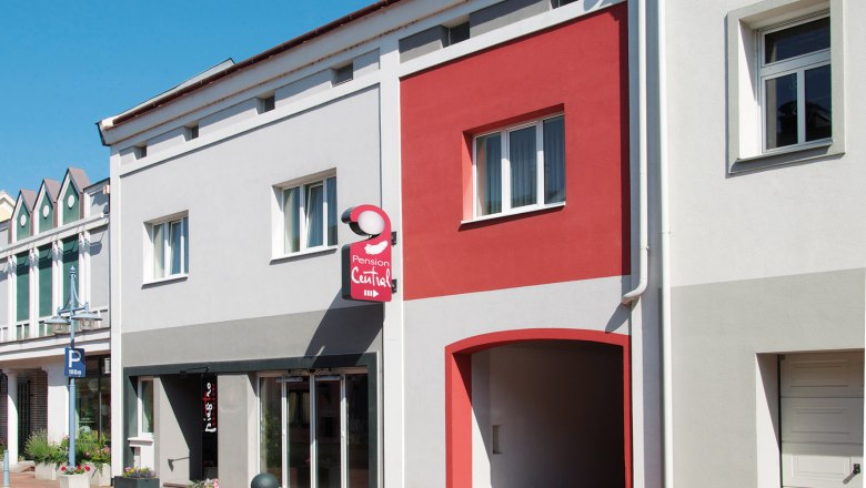 Fassade der Pension Central mit grauen und roten Wänden, einem Schild und Fenstern.