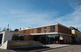 Modernes Geb&auml;ude mit Holzfassade und Glasfront, davor ein Schild mit der Aufschrift 'Fromwald'.