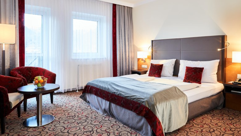 Doppelzimmer im Hotel Schneeberghof mit Doppelbett, roten Kissen, Tisch mit Obstschale und zwei Sesseln.