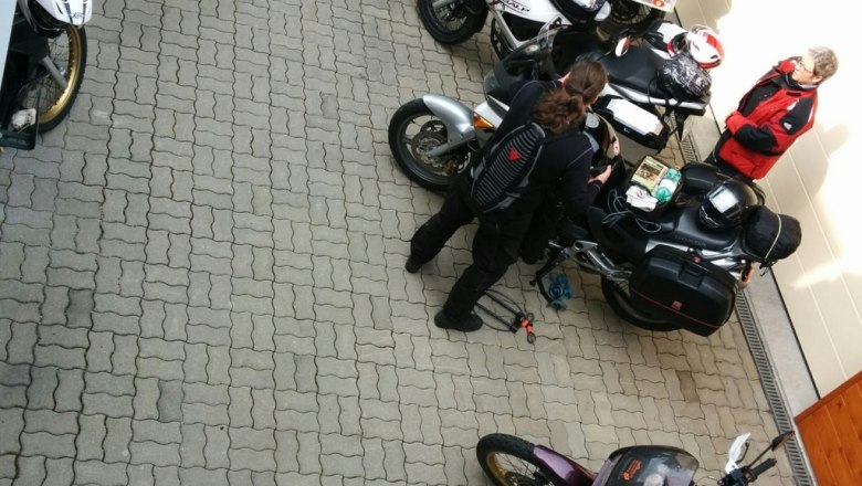 Mehrere Motorräder und Personen auf einem gepflasterten Platz vor einem Gebäude.