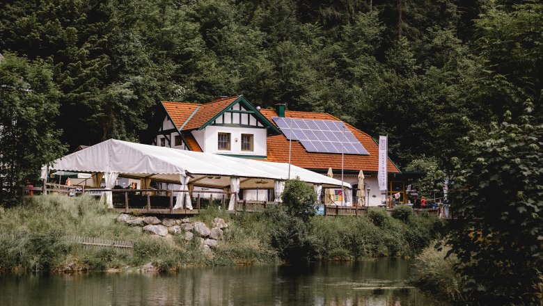 Gasthaus mit Solarpanelen und Zelt am Waldrand, nahe einem Teich.