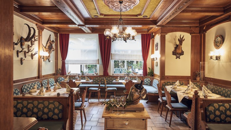 Gemütliche Jägerstube mit Holzmöbeln, Jagdtrophäen an den Wänden und gedeckten Tischen.