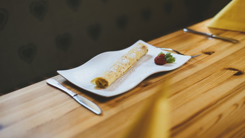 Eine Palatschinke auf einem weißen Teller mit Erdbeere und Minze, auf einem Holztisch serviert.