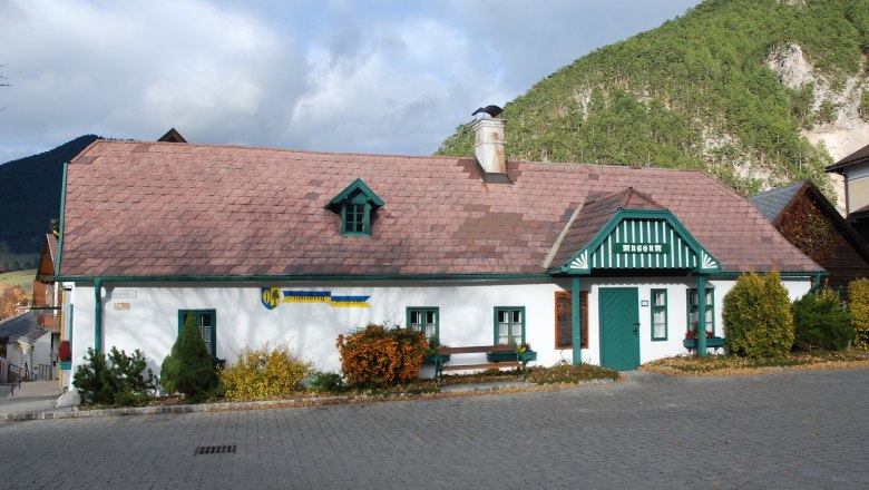 Schneebergmuseum Puchberg, ein traditionelles Gebäude mit grünem Dach und Schornstein, umgeben von Bergen und Bäumen.