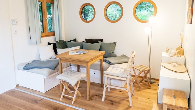 Gemütlicher Sitzbereich mit Holztisch, Stühlen und runden Fenstern.