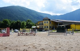 Reitstall Halmerhof mit Springplatz und Bergen im Hintergrund.