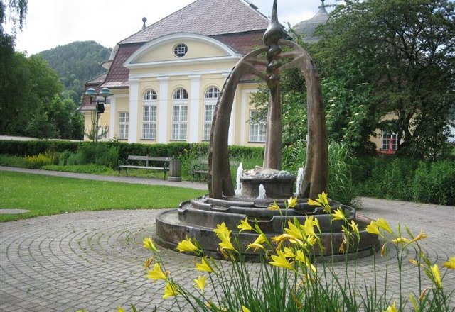 Brunnen vor einem historischen Gebäude mit gelben Blumen im Vordergrund.