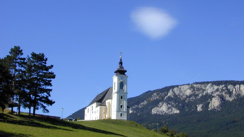 Kirche auf einem H&uuml;gel mit blauem Himmel und Bergen im Hintergrund.