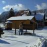 Winterlandschaft mit schneebedecktem Haus und Bergen im Hintergrund.