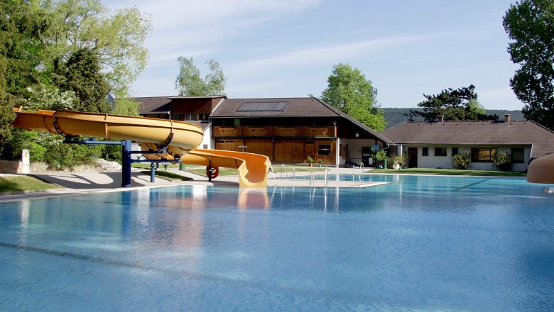 Ein Freibad mit Rutsche und Gebäuden im Hintergrund.